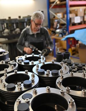 Pressringe mit Zusatzbohrung liegen auf Tisch. Mann im Hintergrund zieht bei einem Pressring Schraube an.