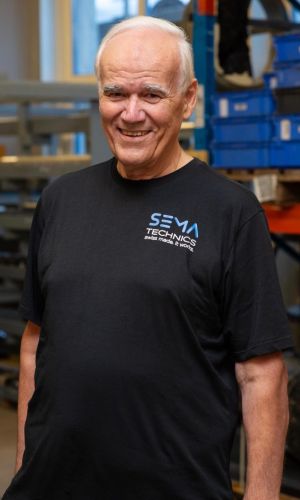 Rolf Keller mit Sema Technics AG Shirt porträtiert vor Gestell mit Pressringen.