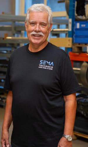 Köbi Debrunner mit Sema Technics AG Shirt porträtiert vor Gestell mit Pressringen.