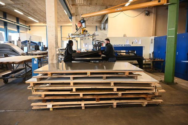 Zwei Männer heben Metallplatte auf eine Maschine.